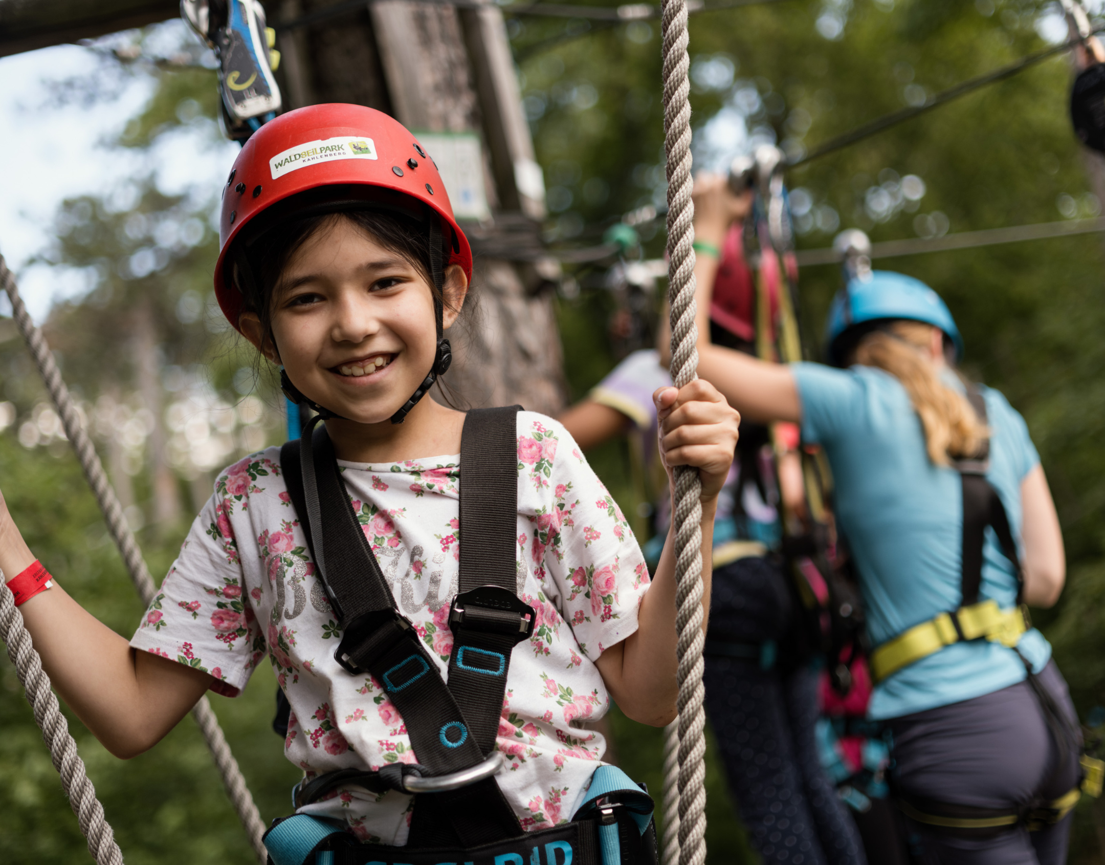 Mädchen mit rotem Helm, lächelnd, beim Klettern in einem Abenteuerpark.