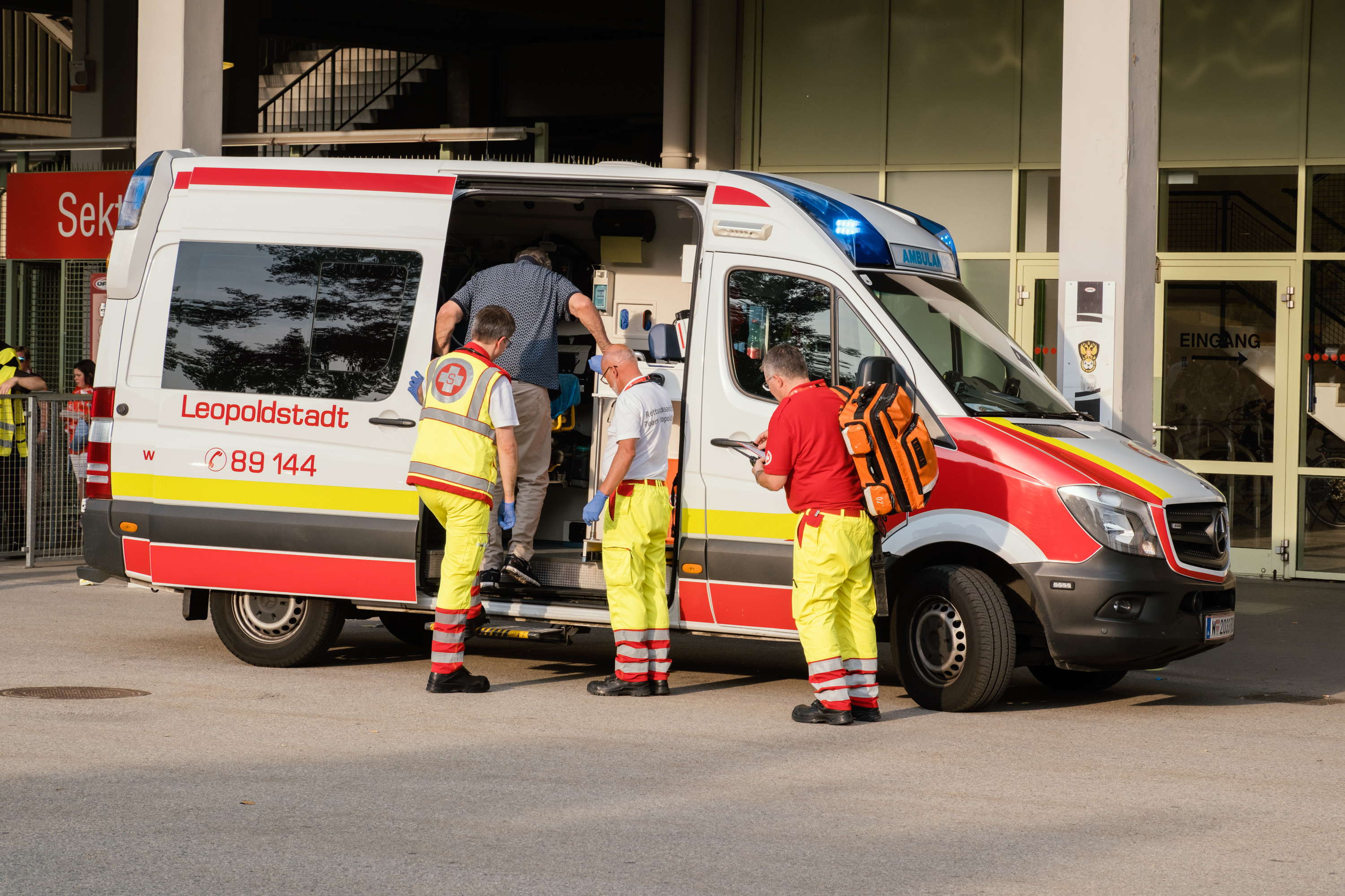 Patient betritt Rettungsauto bei Ernst-Happel-Stadion und drei Rettungssanitäter stehen vor dem Auto
