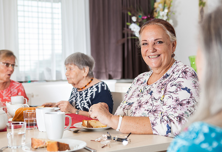 Vier Bewohnerinnen sitzen beim Frühstück, eine Frau lächelt in Kamera