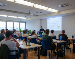 Gruppe von Menschen sitzt in einem Besprechungssaal, Beamer mit Powerpoint-Präsentation