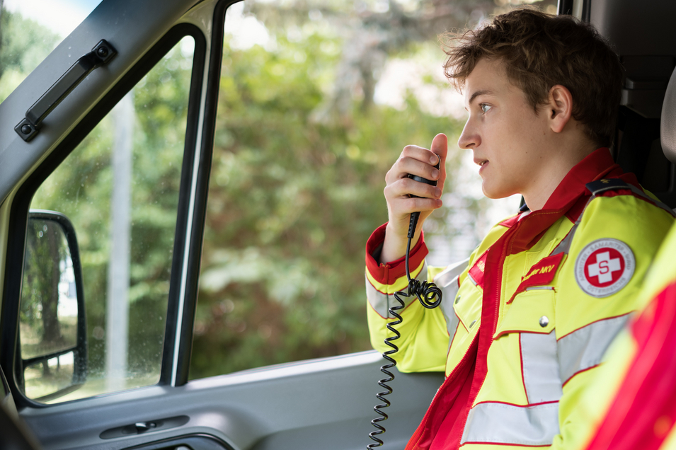 Ehrenamtlicher Rettungssanitäter spricht am Funkgerät und sitzt im Auto