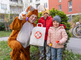 Osterhase mit Kindern in einem Hof, alle lächeln in Kamera, Kinder halten bunte Eier in der Hand