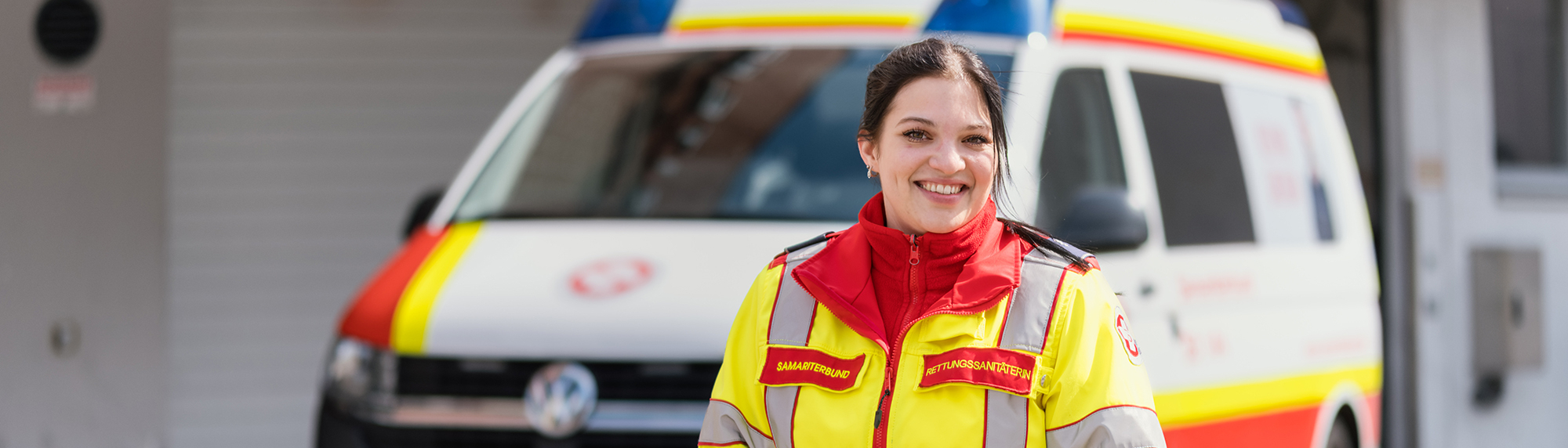 Berufsmodul – Sanitäterin steht vor Krankentransportwagen und lächelt in die Kamera