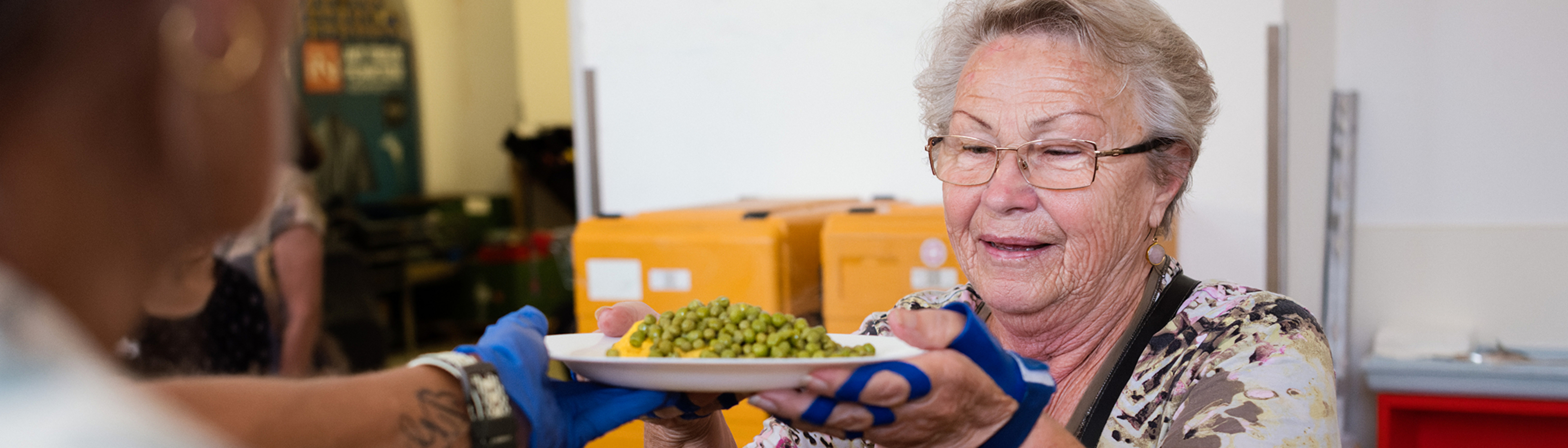 ältere Dame mit Brille bei Samariter Suppentopf Essenausgabe, nimmt Teller mit Essen entgegen