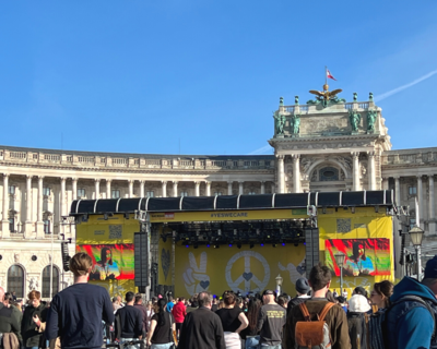 Bühne vor Heldenplatz, Menschen davor, von hinten fotografiert, blauer Himmel und Sonnenschein