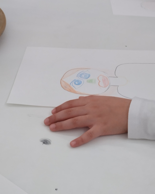 Ein Bild wird gerade von einem Kind gemalt. Die linke Hand ruht neben dem Bild.