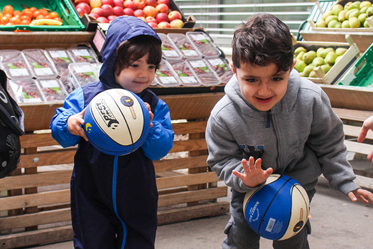 zwei kleine Jungs stehen vor Gemüse in Sozialmarkt und freuen sich über ihre neuen Fußbälle