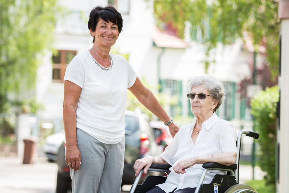 Mitarbeiterin von Besuchsdienst macht Spaziergang mit Dame im Rollstuhl