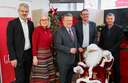 Fünf Personen stehen um einen Weihnachtsmann vor einem festlich geschmückten Baum.