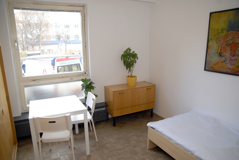 WohnenPlus Riga - Ansicht Einzelzimmer mit Sideboard, Tisch und Bett
