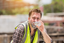 Ein Bauarbeiter in einer Warnweste sitzt und trinkt Wasser aus einer Flasche an einem sehr heißen Tag.