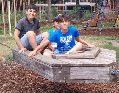 drei Kinder sitzen in Boot aus Holz, Spielplatz