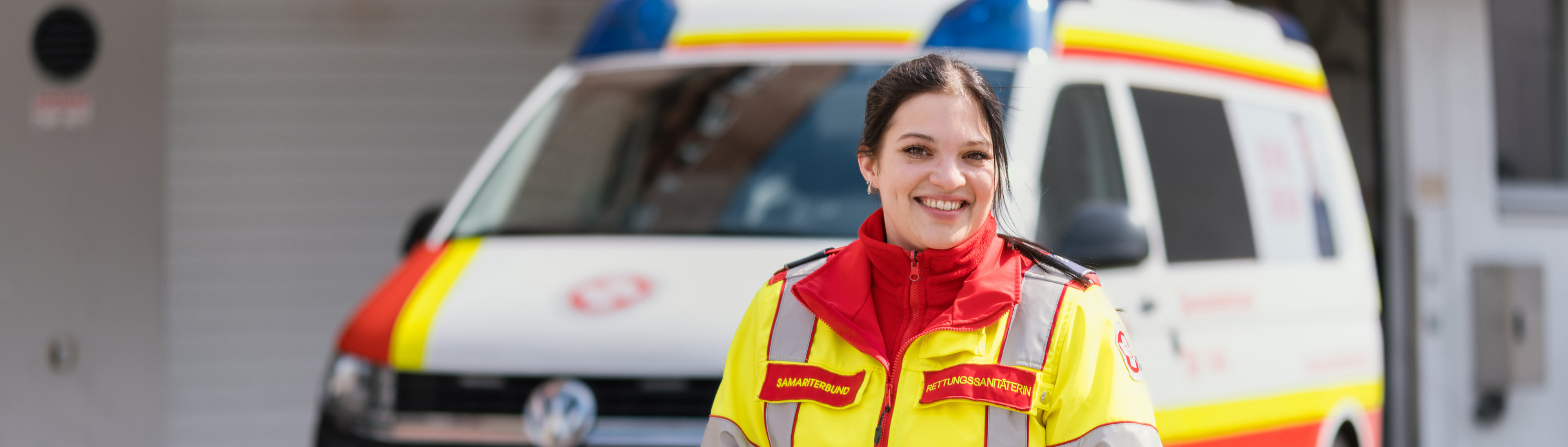 Rettungssanitäterin vorne, Krankentransportwagen im Hintergrund
