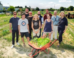 Eine Gruppe von Personen steht auf einem Feld. Vor ihnen steht eine Schubkarre, gefüllt mit Salat.