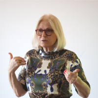 Eine Frau mit kurzen blonden Haaren und Brille unterhält sich mit jemanden.