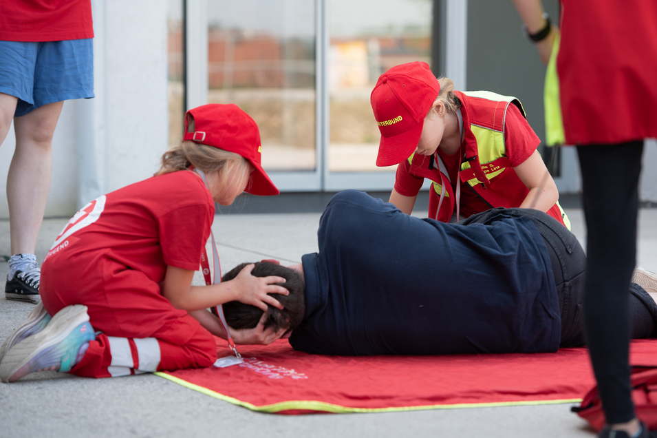 Zwei Kinder leisten Erste Hilfe an einer hilflosen Person auf dem Boden.