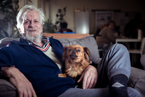 Grauhaariger Mann sitzt mit seinem kleinen Hund am Schoß auf einem Sofa