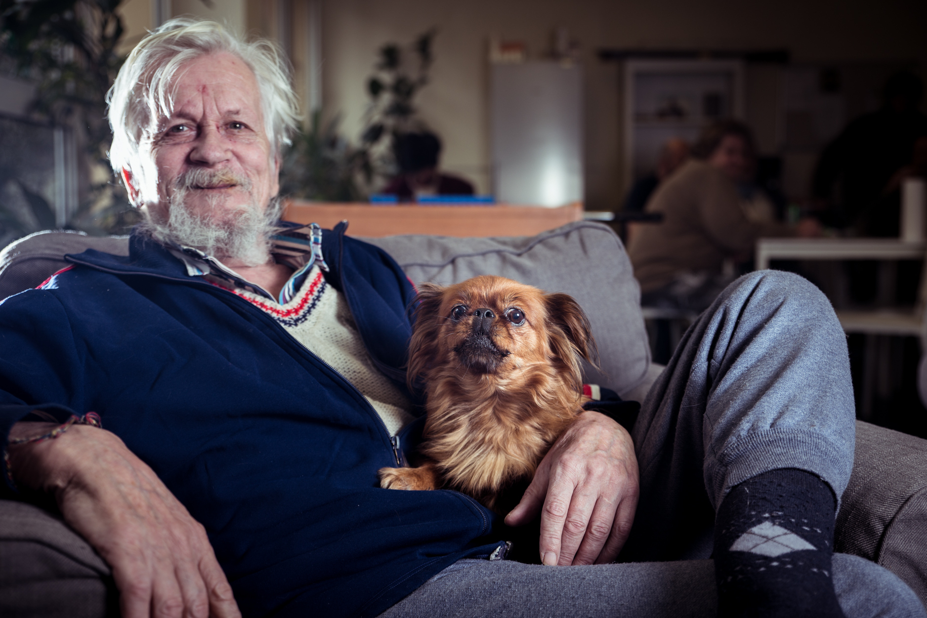 Bewohner einer Wohnungsloseneinrichtung mit Hund am Schoß auf Sofa