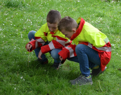 Zwei Jungen mit Einsatzuniform knien am Boden im Gras