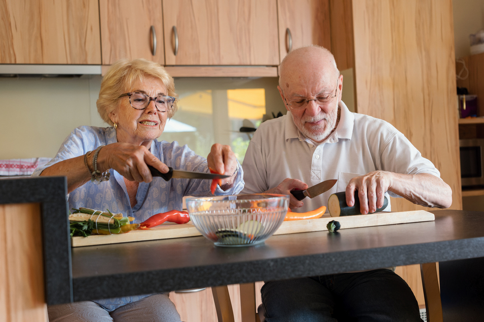 Eine Seniorin und ein Senior schneiden gemeinsam Gemüse in der Küche