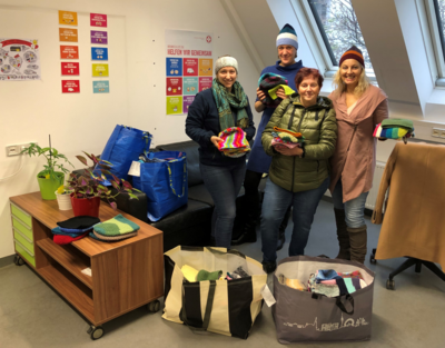 Vier Personen stehen in einem Raum mit großen Taschen, die voll mit Hauben sind. Sie halten auch Hauben in der Hand. 