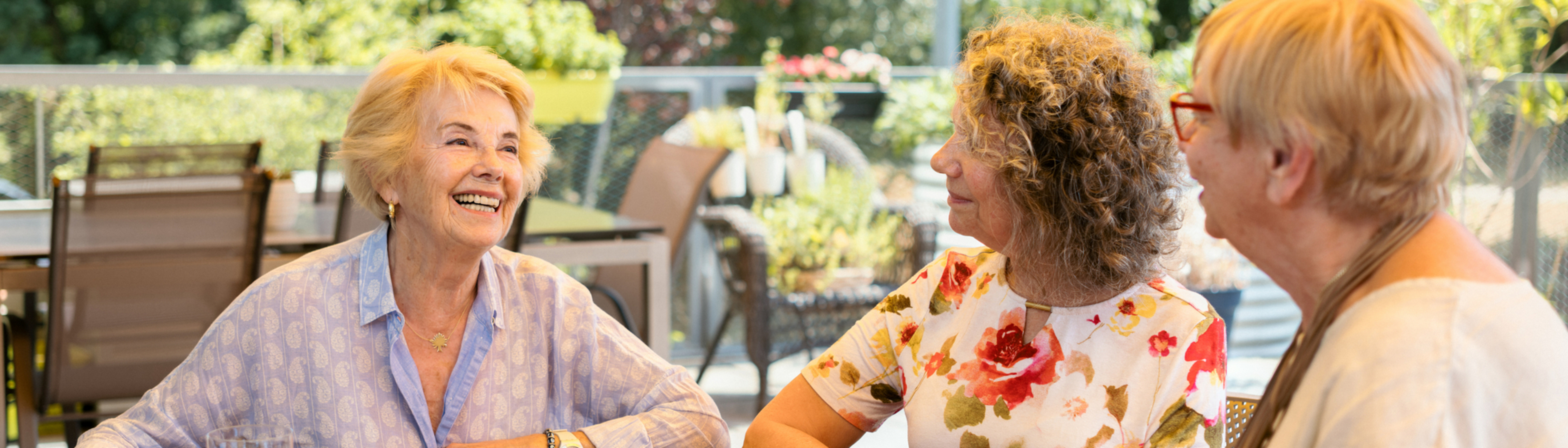 Drei Damen sitzen bei Kaffee und Kuchen auf der Terrasse zusammen und unterhalten sich herzhaft