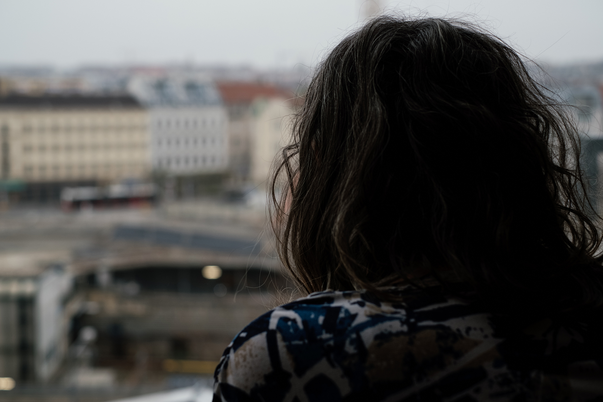 Frau von hinten fotografiert, blickt aus Fenster im Hintergrund verschwommen Häuser, Stadtbild