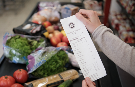 Zwei Hände halten eine Einkaufsrechnung vor einem vollen Kassenband, Sozialmarkt, Einkauf