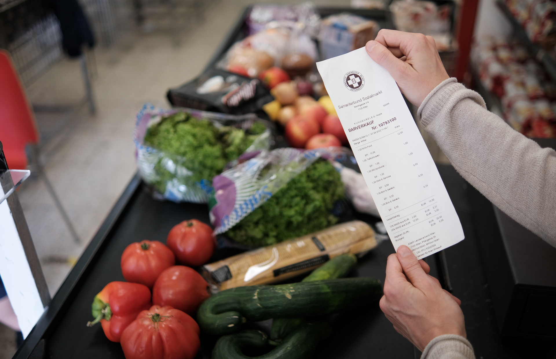 Fleißband in Supermarkt mit Gemüse belegt und Kassenbon in der Hand von Kundin