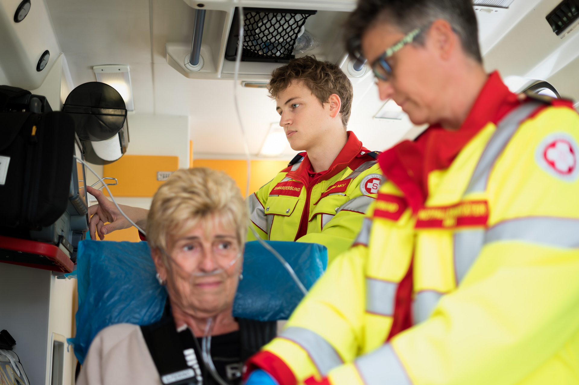 Innenaufnahme von Krrankenwagen in dem sich eine Patientin, eine Sanitäterin und ein Sanitäter befinden