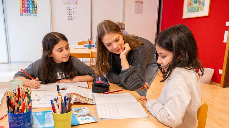 Drei Kinder lernen mit einer Lehrerin an einem Tisch in einem Lernraum.