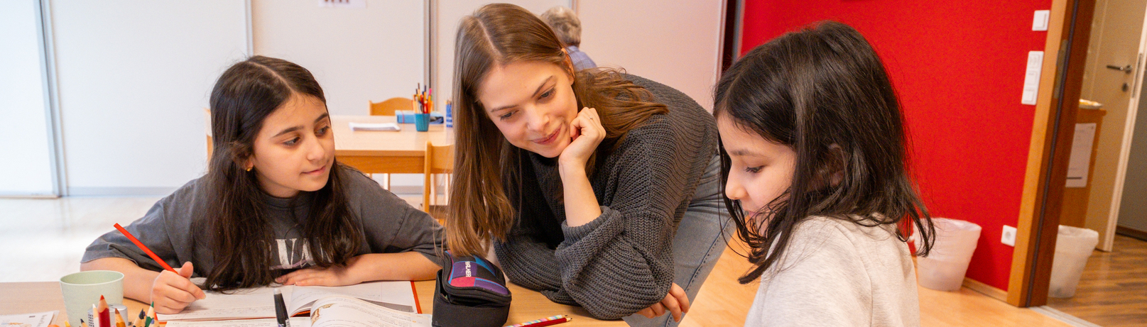 Drei Kinder lernen mit einer Lehrerin an einem Tisch in einem Lernraum.