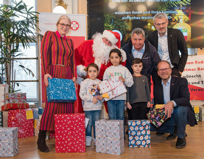 Der Bezirksvorsteher, die Präsidentin vom Samariterbund, der Geschäftsführer vom Samariterbund, der Weihnachtsmann posieren mit Kinder die Weihnachtsgeschenke bekommen haben für eine Foto.