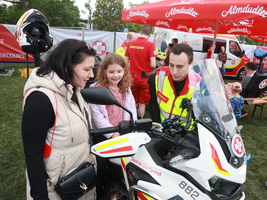 Eine Frau zeigt einer kleinen Tochter ein Motorrad des Samariterbundes. Daneben ein Rettungssanitäter in Uniform. 