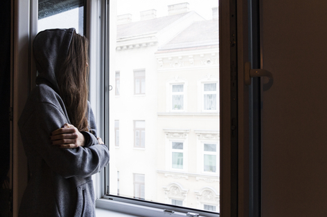 Frau mit Hoodie steht bei offenem Fester und sieht raus