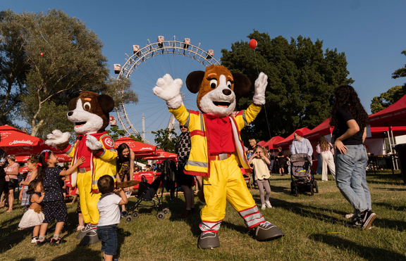 Figuren Sam und Rita tanzen mit Kindern vor dem Wiener Riesenrad