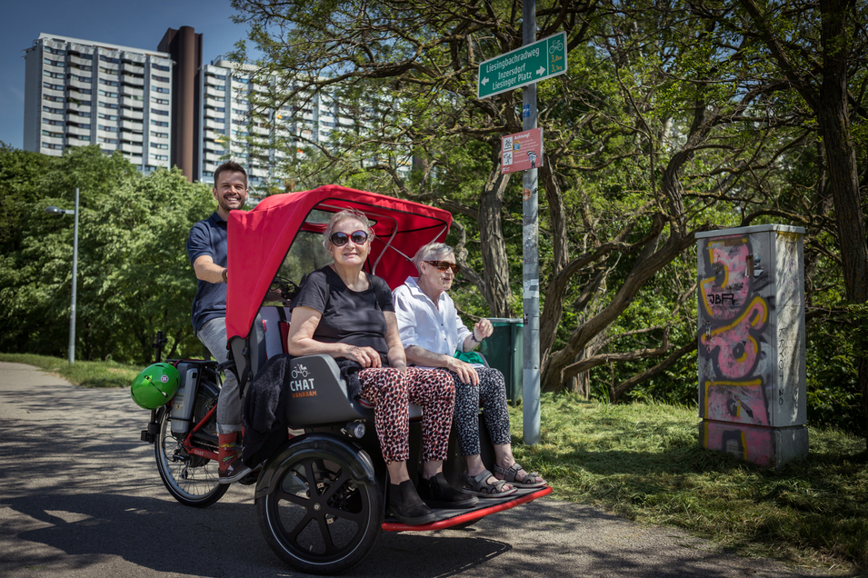 Drei Personen in einem Fahrrad-Rickshaw auf einem grünen Weg.