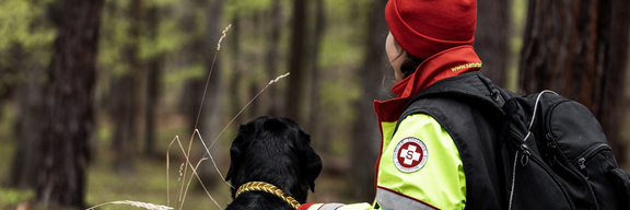 Rettungshund und Trainerin von hinten im Wald