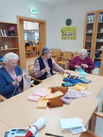 Drei Frauen stricken gemeinsam an einem Tisch, umgeben von bunten Garnen.