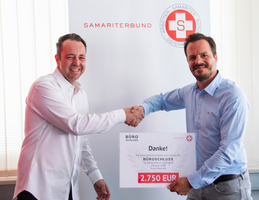 Zwei Männer schütteln sich die Hände und halten ein Dankesschild für eine Spende.