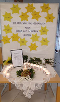 Gedenktisch mit Kerzen, Blumen und gelben Sternen für Verstorbene, mit Trauerbotschaft.