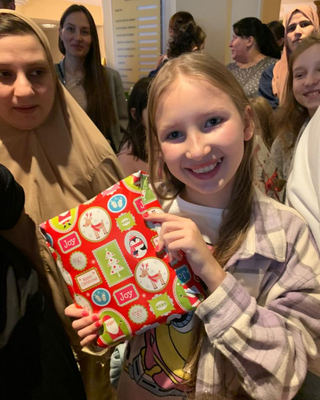 Ein Mädchen hält freudestrahlend ein verpacktes Geschenk in die Kamera.