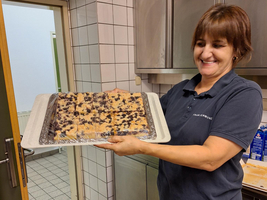 Eine Frau steht in einer Küche und hält ein Kuchenblech in der Hand, auf welches sie hinablächelt. 