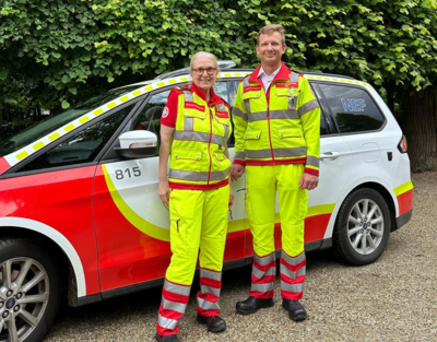 Präsidentin des Samariterbundes in Uniform vor Einsatzwagen, neben ihr steht ein Mann in Uniform