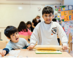 zwei Buben in LernLEO, einer rollt Keksteig aus, beide blicken in Kamera, im Hintergrund weitere LernLEO Kinder, Pinnwand mit Zeichnungen