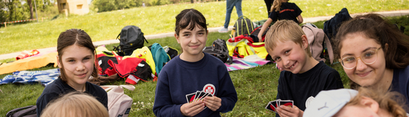 Mehrere Kinder der Samariterjugend sitzen auf einer Picknickdecke und spielen UNO im Park