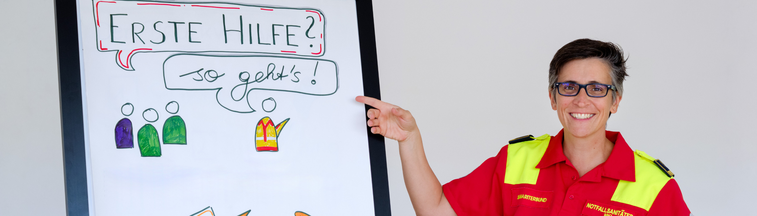 Frau in roter Uniform erklärt Erste Hilfe an Flipchart.