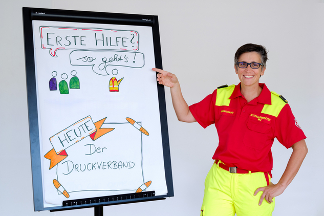 Frau in roter Uniform erklärt Erste Hilfe an Flipchart.