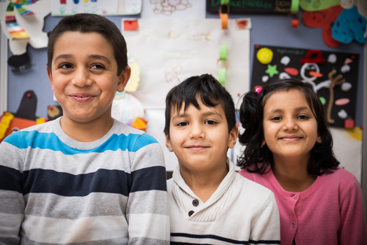 Drei lächelnde Kinder stehen vor bunten Bastelarbeiten.