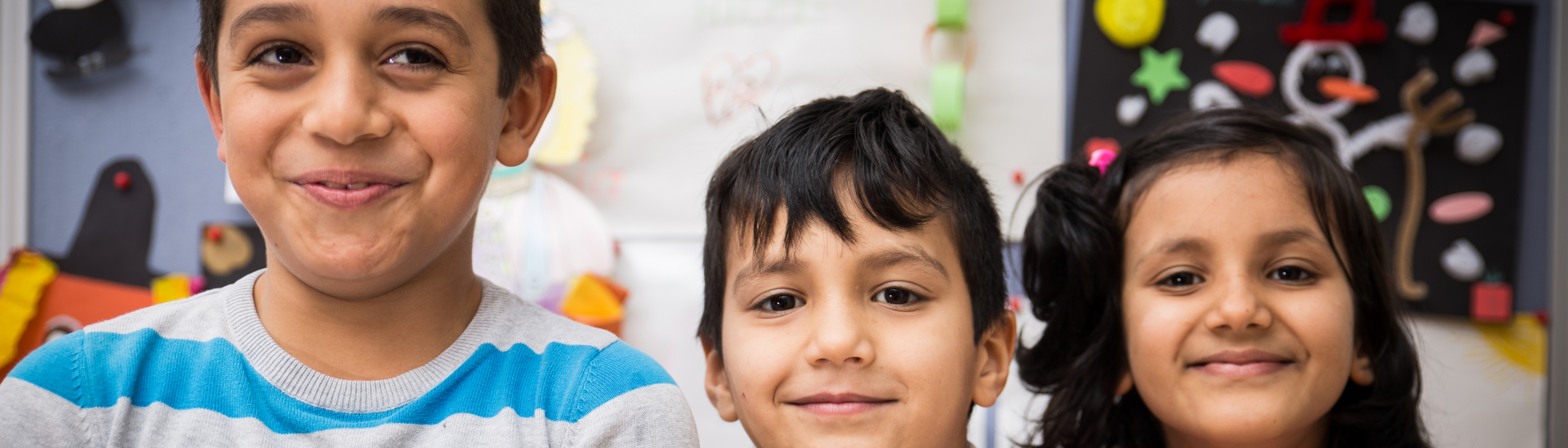 Drei lächelnde Kinder stehen vor bunten Bastelarbeiten.